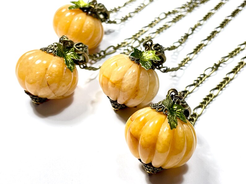 May include: Four pumpkin-shaped pendants on chains. The pumpkins are a light orange color with vertical ridges. Each pumpkin has a decorative metal cap with green leaves. The chains are a bronze color.