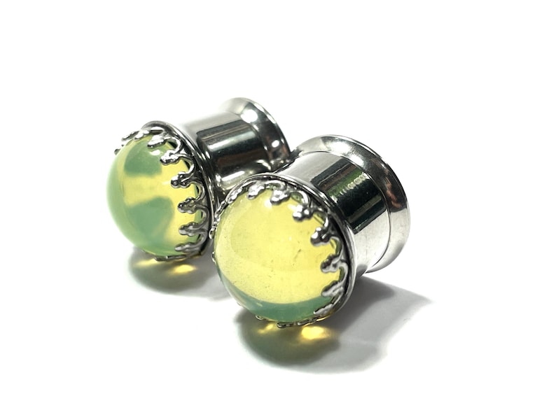 May include: Pair of stainless steel ear gauges with a green stone inlay and a decorative silver trim.