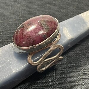 May include: A silver ring with a pink and white oval gemstone set in a silver bezel. The ring band is twisted and has a textured finish.