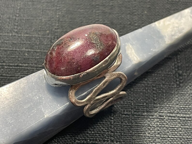 May include: A silver ring with a pink and white oval gemstone set in a silver bezel. The ring band is twisted and has a textured finish.