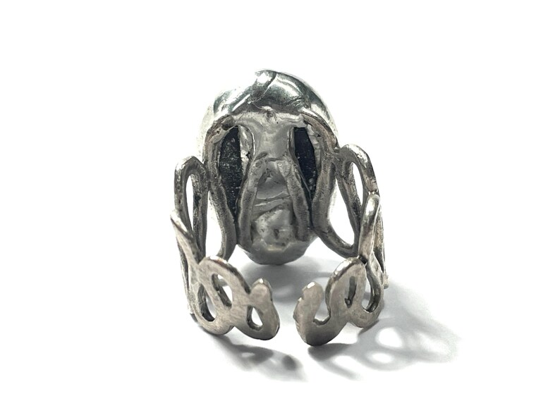 May include: A silver ring with a detailed skull design. The ring is open and adjustable.