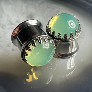 May include: A pair of silver ear gauges with a green stone inlay and a decorative crown design.