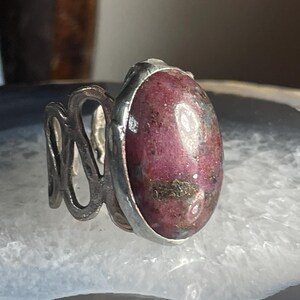 May include: A silver ring with a pink and grey oval gemstone set in a silver band.