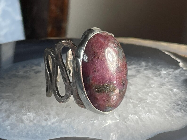 May include: A silver ring with a pink and grey oval gemstone set in a silver band.