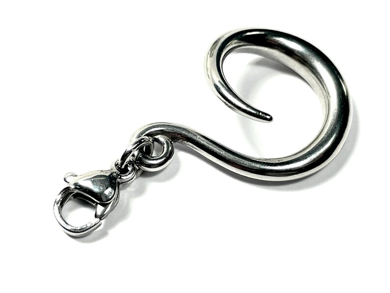 May include: A silver-colored, curved hook with a lobster clasp. The hook has a smooth, polished finish and a rounded, spiral shape. The clasp is attached to the hook with a small ring. The hook is designed to be used for hanging items.