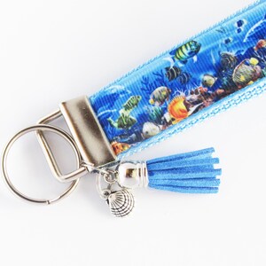 May include: A blue and white key chain with a colorful fish print, a silver key ring, a blue tassel, and a silver seashell charm.