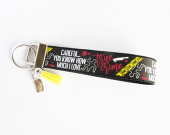May include: Black and yellow keychain with a black ribbon that says "CAREFUL... YOU KNOW HOW MUCH I LOVE TRUE CRIME" with a yellow tassel and a silver knife charm.