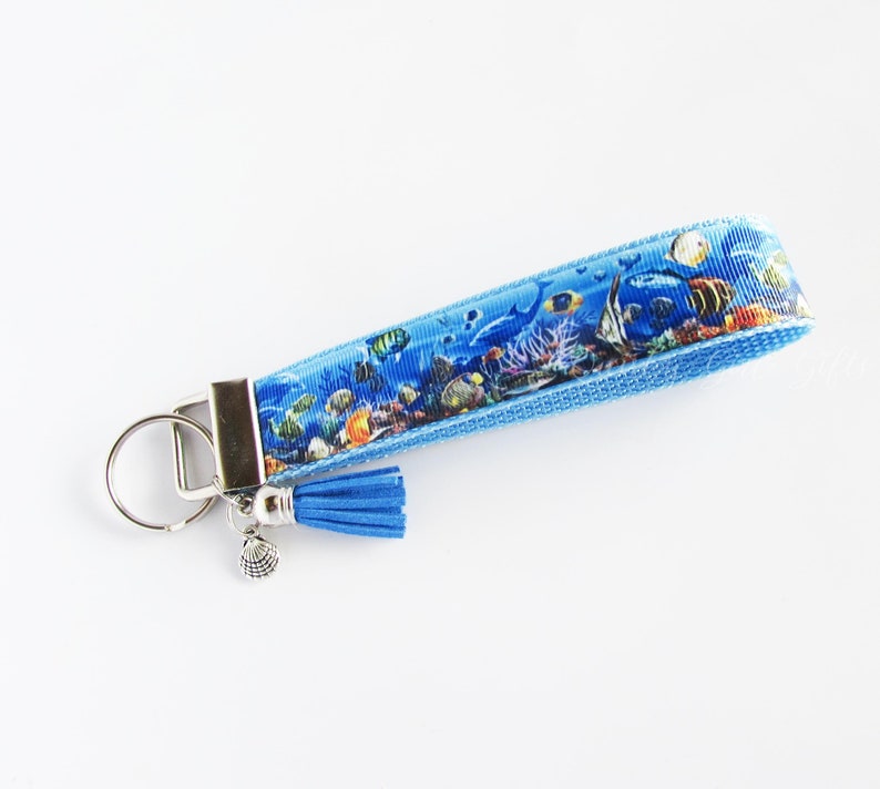 May include: A blue key chain with a colorful fish and coral reef design. The key chain has a silver key ring and a blue tassel.
