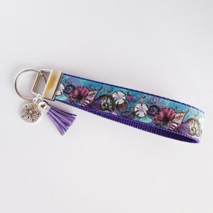 May include: Purple and blue key chain with a seashell design and a silver charm. The charm is a starfish with a small tassel.