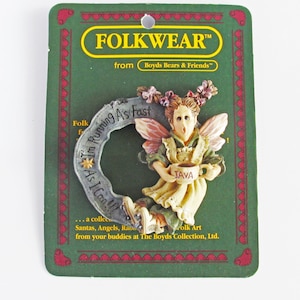 May include: A whimsical fairy figurine with pink wings, holding a coffee cup that says "JAVA". The fairy is wearing a green dress and a white apron. The figurine is on a green card with the text "FOLKWEAR™ from Boyds Bears & Friends™" and "I'm Running As Fast As I Can!"