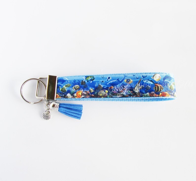 May include: A blue and white key chain with a colorful fish and coral reef design. The key chain has a silver key ring and a blue tassel.