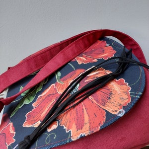 May include: A burgundy crossbody bag with a flap closure. The flap is made of dark blue fabric with a floral print of red poppies. The bag has a black tassel.