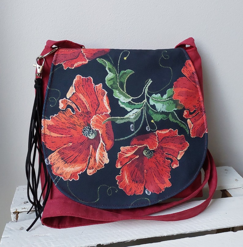 May include: A red and black floral print crossbody bag with a long black tassel. The bag features a large poppy flower design.