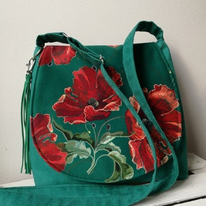 May include: A green suede shoulder bag with a floral print featuring red poppies. The bag has a long strap and a tassel.