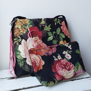 Può includere: Una borsa tote nera in tessuto di tappezzeria floreale con un fiocco rosa e una pochette più piccola abbinata. La borsa presenta un grande motivo floreale con fiori rosa, rossi e gialli.