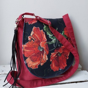 May include: A red crossbody bag with a black floral print featuring red poppies. The bag has a long strap and a black tassel.