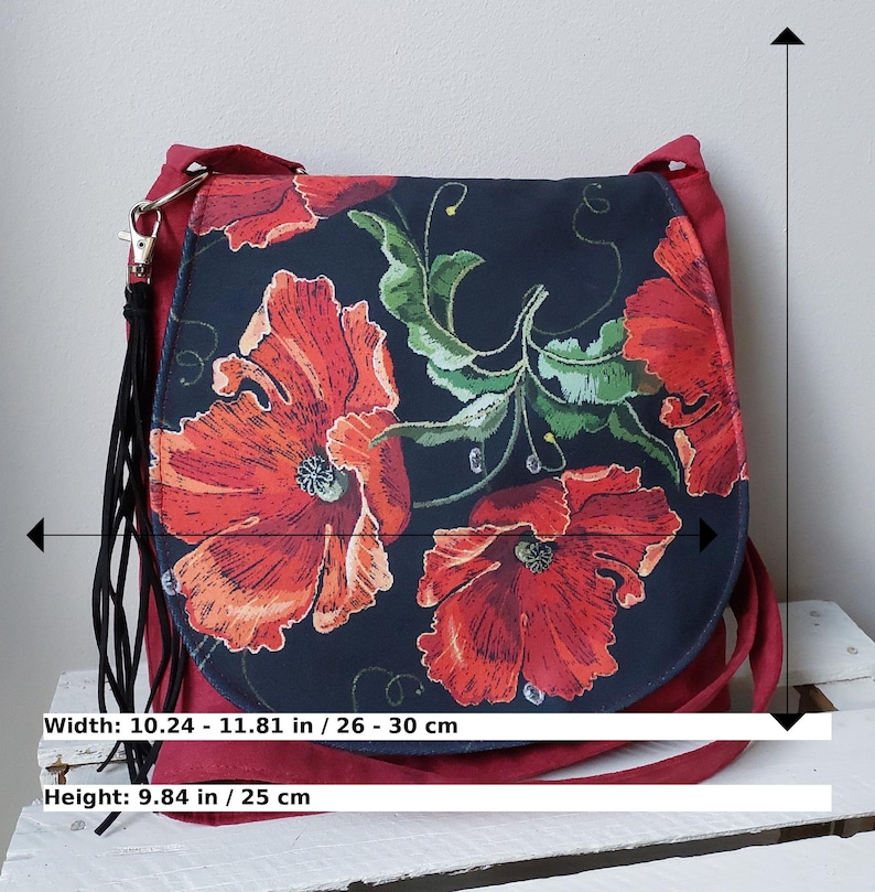 May include: A red suede crossbody bag with a black fabric flap featuring a floral design of red poppies on a black background. The bag measures 10.24 to 11.81 inches wide and 9.84 inches high.