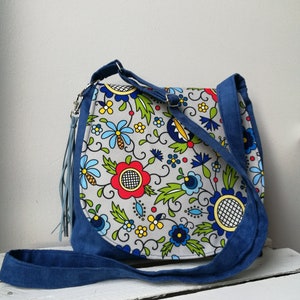 May include: A gray and blue crossbody bag with a floral pattern. The bag has a long strap and a tassel.