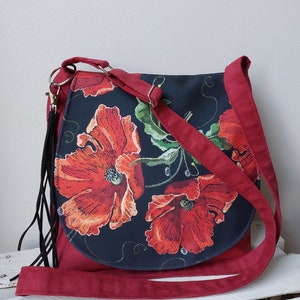 May include: A red suede crossbody bag with a black fabric flap featuring a floral design of red poppies on a black background.