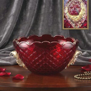 May include: A deep red glass bowl featuring a textured diamond pattern on the exterior and a scalloped rim. The bowl includes two ornate, gold-toned handles shaped like lion heads on opposite sides, matching the lion motif shown in the inset.