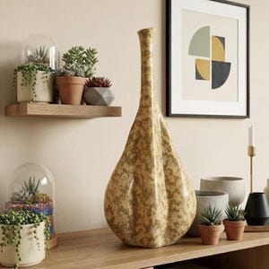 May include: A tall, teardrop-shaped ceramic vase with a mottled tan and beige finish. The vase features a narrow neck and a wide, textured base with subtle vertical indentations. It stands prominently among various small potted succulents and plants.