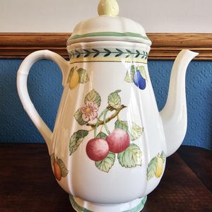 May include: White ceramic teapot with a lid and handle. The teapot is decorated with colourful illustrations of cherries, pears, and plums. The lid has a yellow knob. Green and yellow bands encircle the teapot.