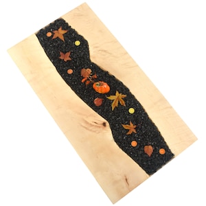 May include: A wooden table top with a black resin river filled with black pebbles, orange and yellow leaves, and small orange pumpkins.