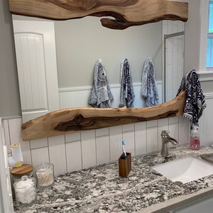 Puede incluir: Un tocador de ba&ntilde;o con un espejo de madera de borde vivo y una encimera blanca. La encimera tiene un patr&oacute;n de granito y cuenta con un lavabo de porcelana blanca, un grifo plateado y un portacepillos de dientes. Hay tres frascos en la encimera, uno con bolas de algod&oacute;n, uno con bastoncillos de algod&oacute;n y uno con una tapa de madera.