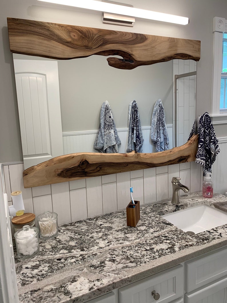 Puede incluir: Un tocador de ba&ntilde;o con un espejo de madera de borde vivo y una encimera blanca. La encimera tiene un patr&oacute;n de granito y cuenta con un lavabo de porcelana blanca, un grifo plateado y un portacepillos de dientes. Hay tres frascos en la encimera, uno con bolas de algod&oacute;n, uno con bastoncillos de algod&oacute;n y uno con una tapa de madera.