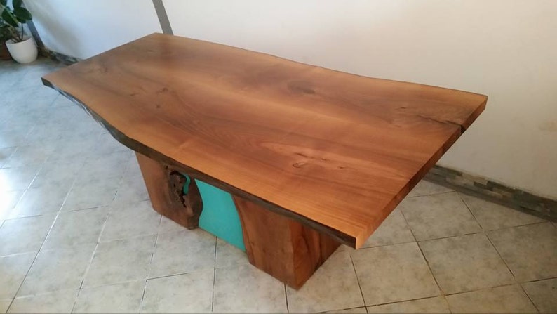 May include: A wooden table with a live edge top and a turquoise epoxy resin inlay. The table is made of natural wood and has a rustic, handmade look.
