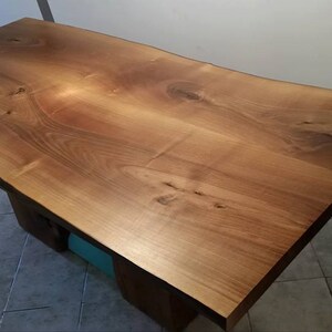 May include: A large, live edge wooden table top with a natural wood finish. The table top is made of a single piece of wood and has a unique, organic shape.