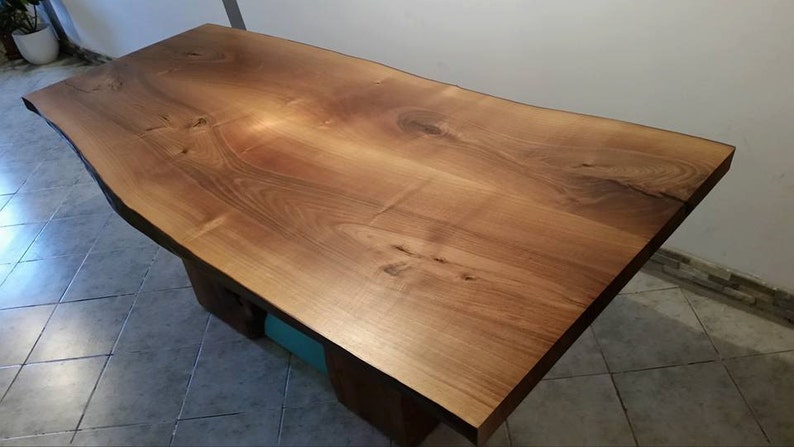 May include: A large, live edge wooden table top with a natural wood finish. The table top is made of a single piece of wood and has a unique, organic shape.