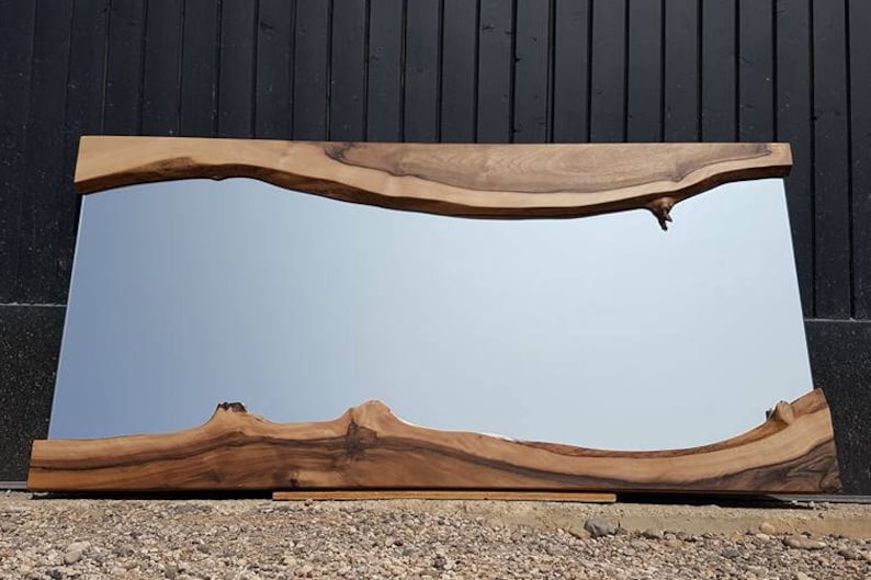 Puede incluir: Un espejo grande y rectangular con un marco de madera natural. El marco tiene una forma org&aacute;nica &uacute;nica con un borde ondulado y nudos en la madera. El espejo refleja un cielo azul claro.