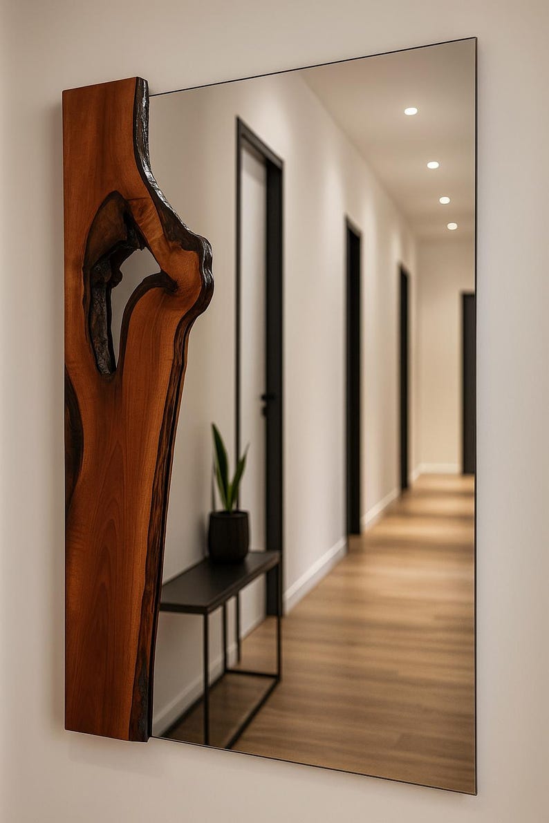May include: A rectangular mirror with a black frame and a natural wood accent on the left side. The wood has a unique, organic shape with a dark, open knot. The mirror reflects a hallway with black doors and a wooden floor.