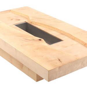 May include: A light wood coffee table with a rectangular cutout in the top. The cutout is surrounded by a raised edge and has a dark gray interior.