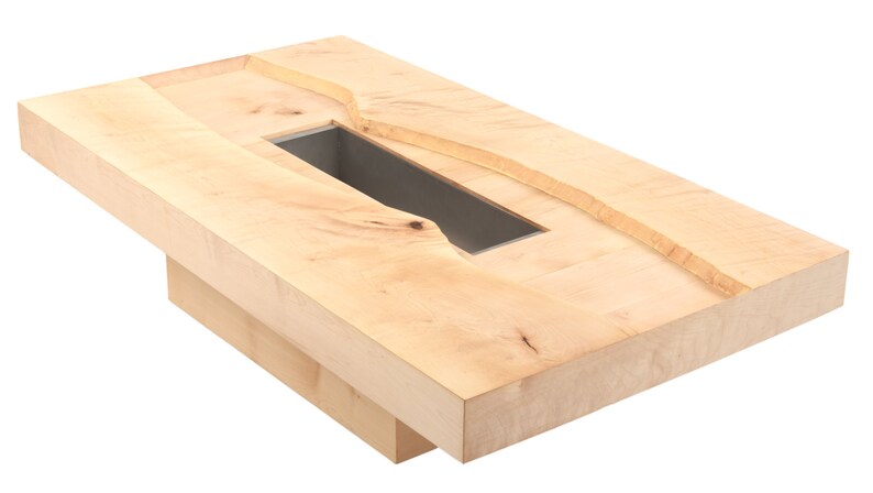 May include: A light wood coffee table with a rectangular cutout in the top. The cutout is surrounded by a raised edge and has a dark gray interior.