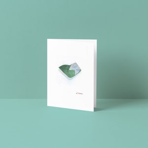Pode incluir: Um cartão branco com uma ilustração em aquarela verde e branca de um pedaço de papel dobrado. O cartão é assinado "L. Mama".