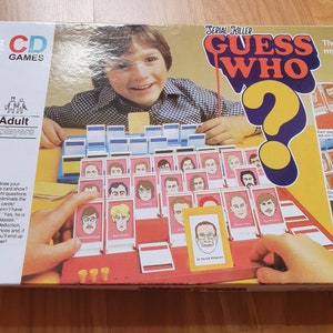 May include: A board game box with a red and yellow design. The game is called "Serial Killer Guess Who?" and features a question mark with a red outline. The box shows a young boy playing the game.