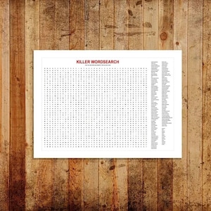 May include: A white framed print featuring a word search puzzle titled "KILLER WORDSEARCH" in red text. The puzzle is filled with black letters and a list of words to find is on the right side. The background is a wooden surface.