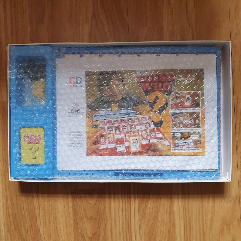 May include: A blue and white board game box with the title "Guess Who?" printed on the front. The box contains a game board, cards, and other game pieces. The game is made by the company "C.D. Games".