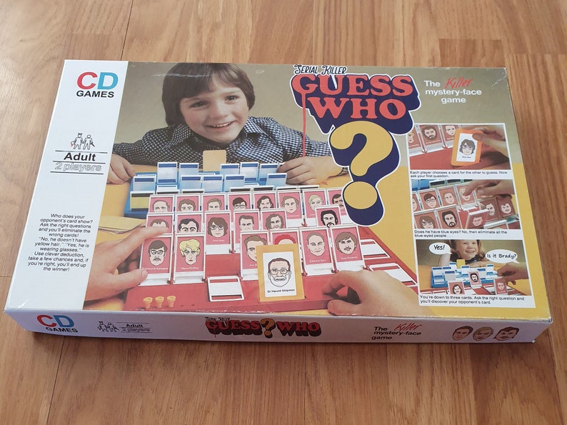 May include: A board game box for the game "Serial Killer Guess Who?" The box is red, white, and blue with a picture of a question mark and a person's face. The game is for adults and has two players. The text on the box says "The Killer mystery-face game."