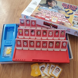 May include: A red and blue game board with the title "Guess Who?" and a variety of faces on cards. The game is set up with a row of cards with faces on them, and a row of cards with question marks on them. The game is designed for adults.