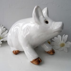 May include: A white ceramic pig figurine with brown accents. The pig is standing on all four legs with its head turned to the side. The figurine is a decorative item.