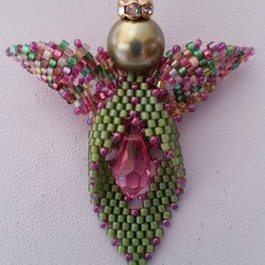 Könnte beinhalten: Ein Perlenengel-Anhänger in Grün- und Rosatönen. Der Engel hat einen Perlenkopf mit einer goldenen Krone und einen rosafarbenen Kristall in der Mitte.