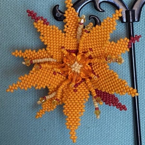 May include: A beaded flower brooch with orange and red petals. The flower is made of small beads and has a central cluster of orange beads.