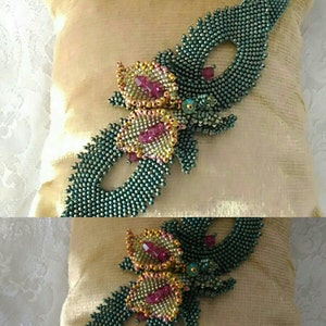 May include: A beaded floral design with green, gold, and pink beads. The design is attached to a cream-colored fabric.
