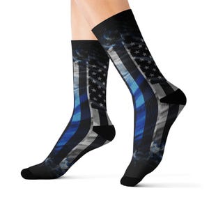 May include: Black socks featuring a design of the American flag with a blue stripe. The socks have a black heel and toe, and the flag design includes stars and stripes. The blue stripe is a prominent feature, and the overall design has a slightly smoky effect.