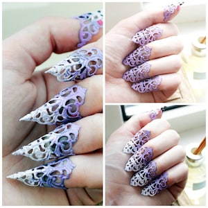 May include: A set of five finger rings with a delicate, lacy design. The rings are made of metal and have a gradient color scheme, transitioning from white to purple.