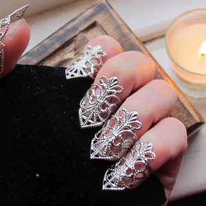 May include: Five silver filigree finger rings with pointed tips. The rings are worn on the fingers of a hand.
