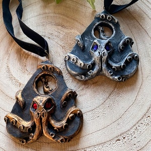 May include: Two black and silver octopus pendant necklaces with red and blue gemstone eyes. The necklaces are on a wooden surface.